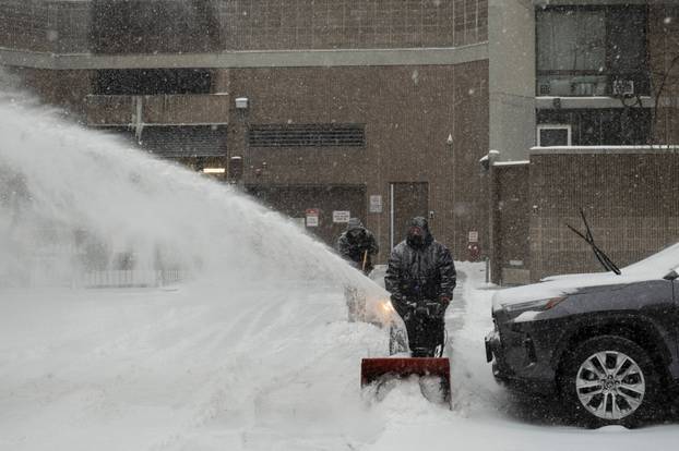 People use blowers to clear snow off walkways, amid a major winter storm spreading across a large swath of the United States, in Brooklyn