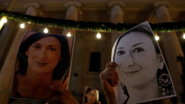 People hold photos of assassinated anti-corruption journalist Daphne Caruana Galizia during a vigil to mark eleven months since her murder in a car bomb, outside the Courts of Justice in Valletta