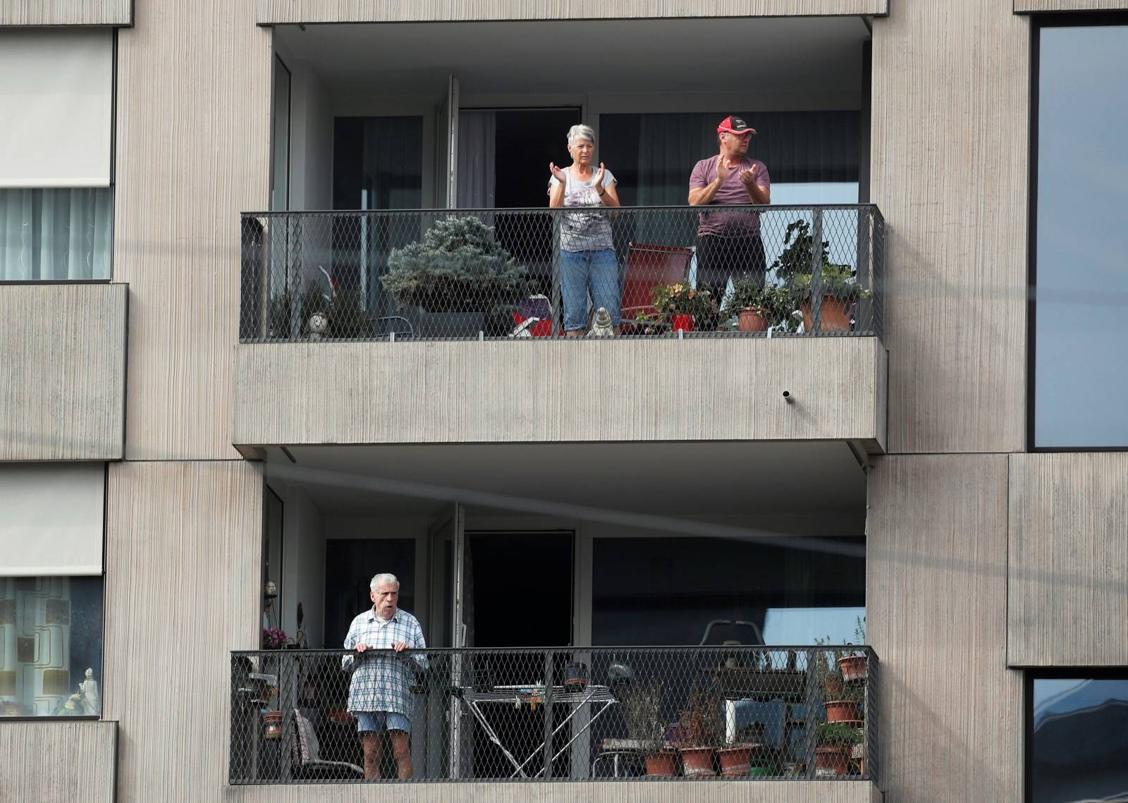 People stand on their balcony and clap as they take part in a Swiss-wide applause for medical teams in Zurich