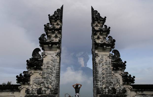 A tourist watches as Mount Agung volcano erupts at Lempuyang Temple in Karangasem, Bali