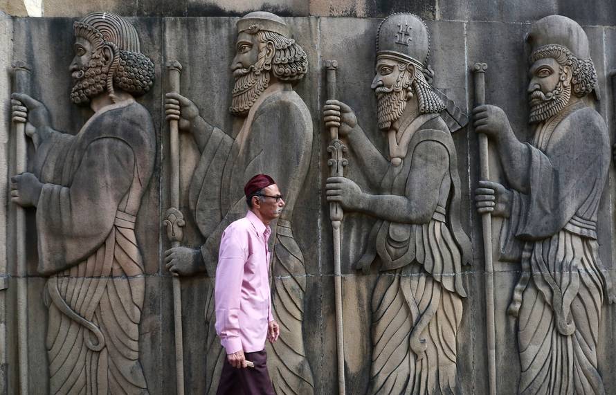 A Parsi man walks past a wall of a Parsi fire temple featuring huge carvings of ancient priests in Mumbai