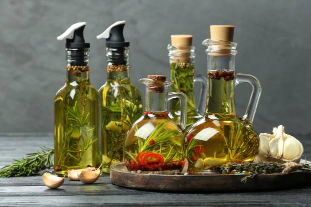 Cooking oil with different spices and herbs in bottles on grey w