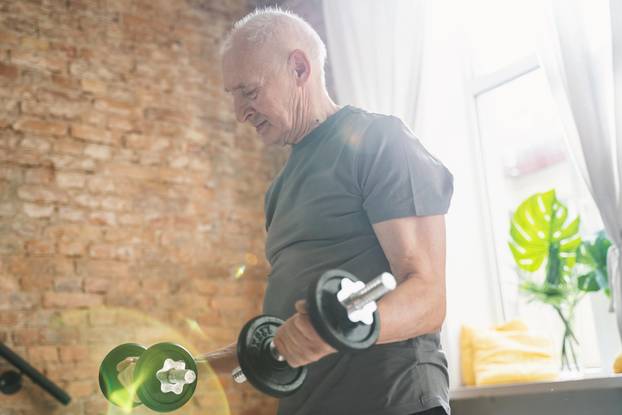 Elderly man exercising with a dumbbells during his workout in home gym