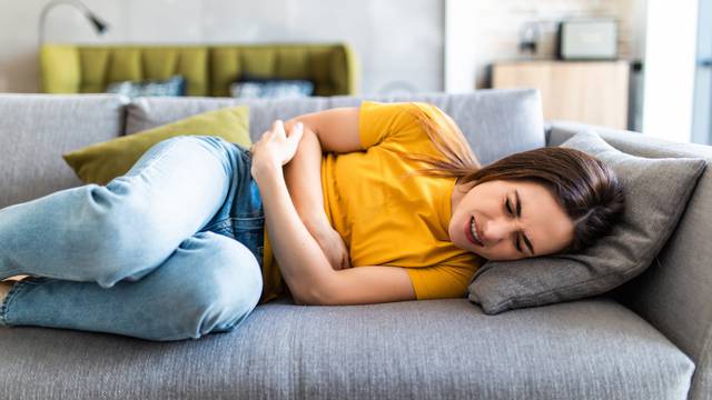 Sick woman lying on sofa in the living room with stomach ache