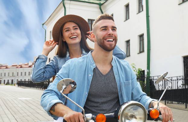 happy young couple riding scooter in town. Handsome guy and young woman travel. Adventure and vacations concept.