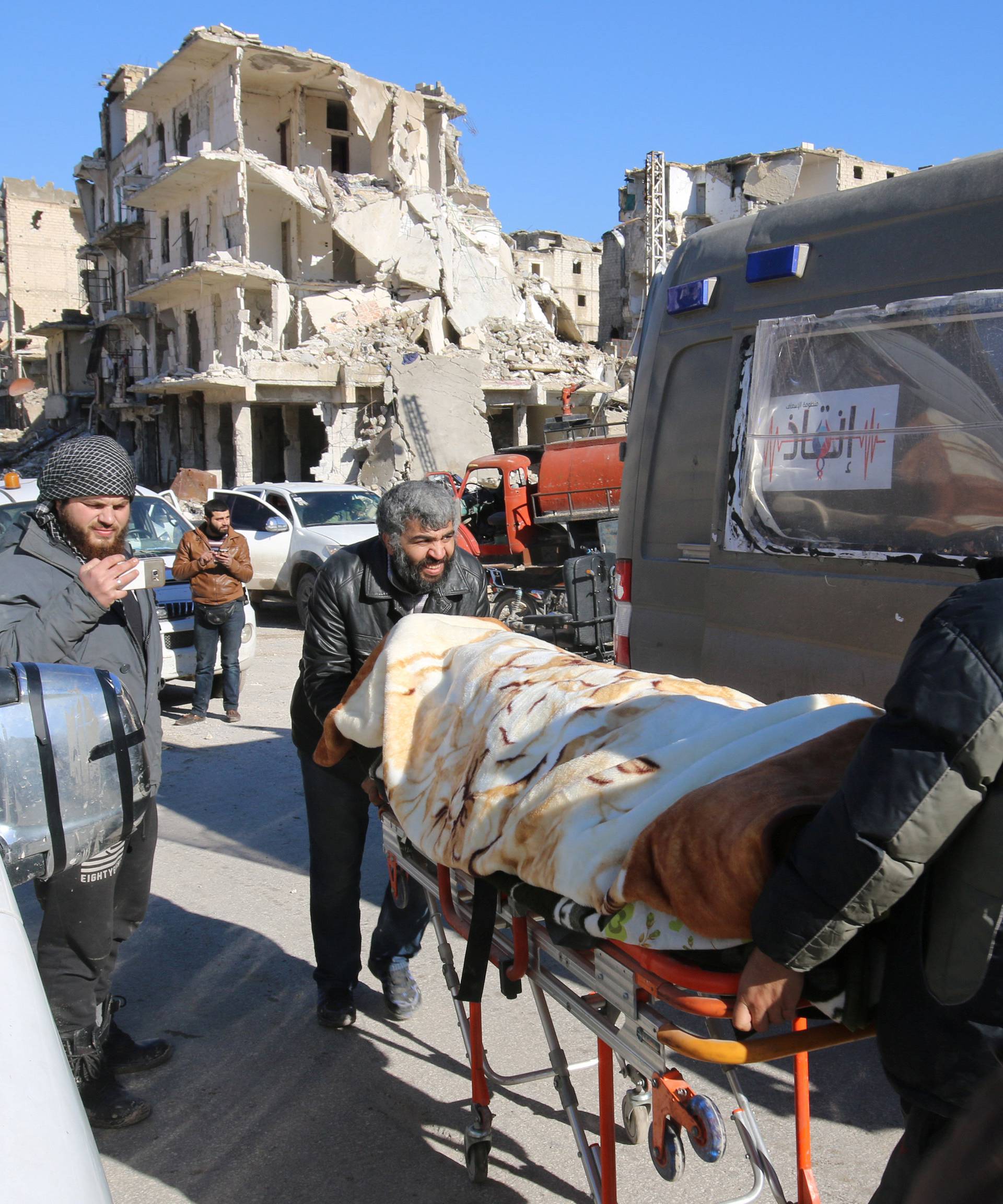 Men push an evacuee on a stretcher as vehicles wait to evacuate people from a rebel-held sector of eastern Aleppo