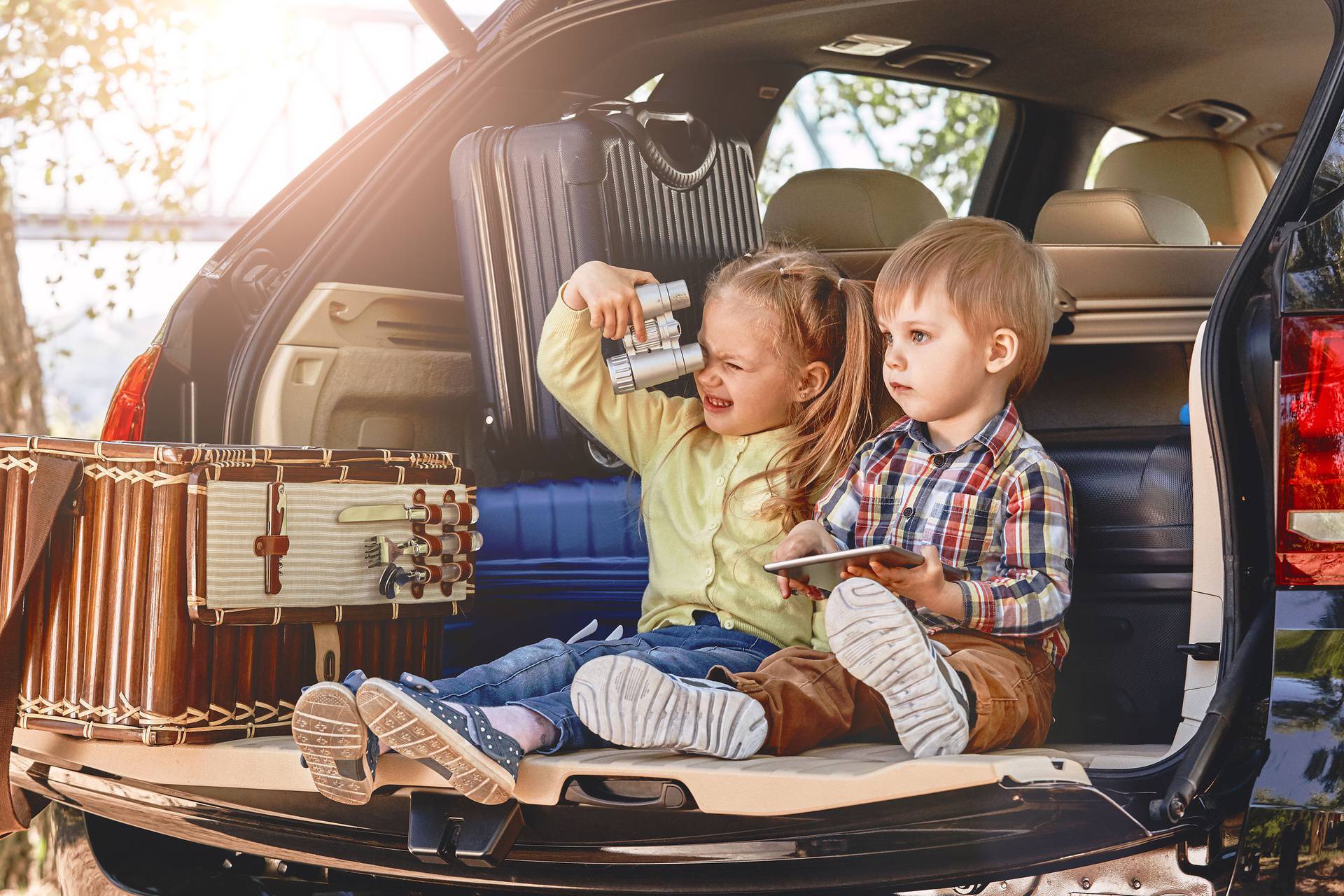 Little cute kids having fun in the trunk of a car with suitcases. Family road trip