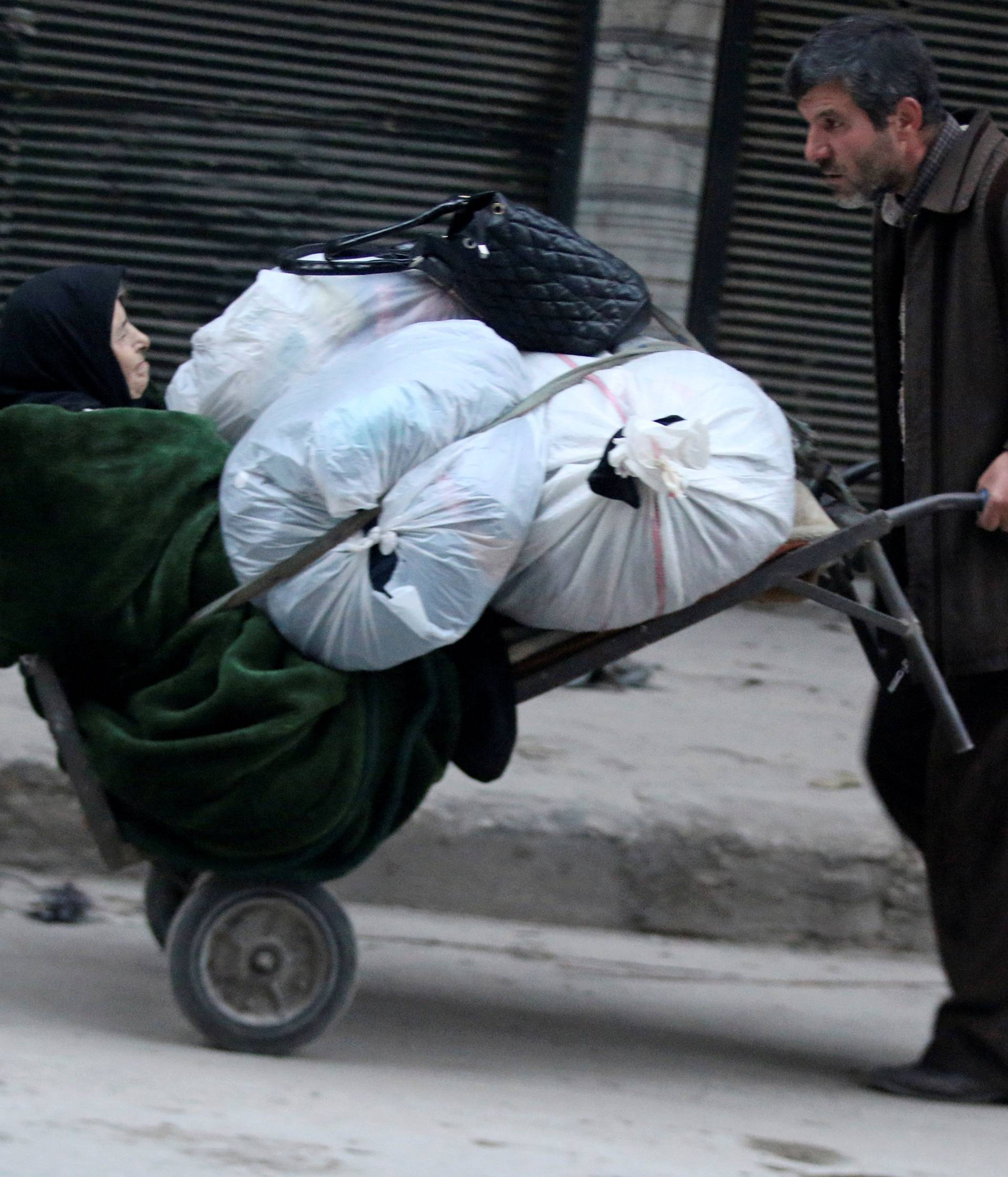 A man pushes a cart carrying an elderly woman and belongings as they flee deeper into the remaining rebel-held areas of Aleppo