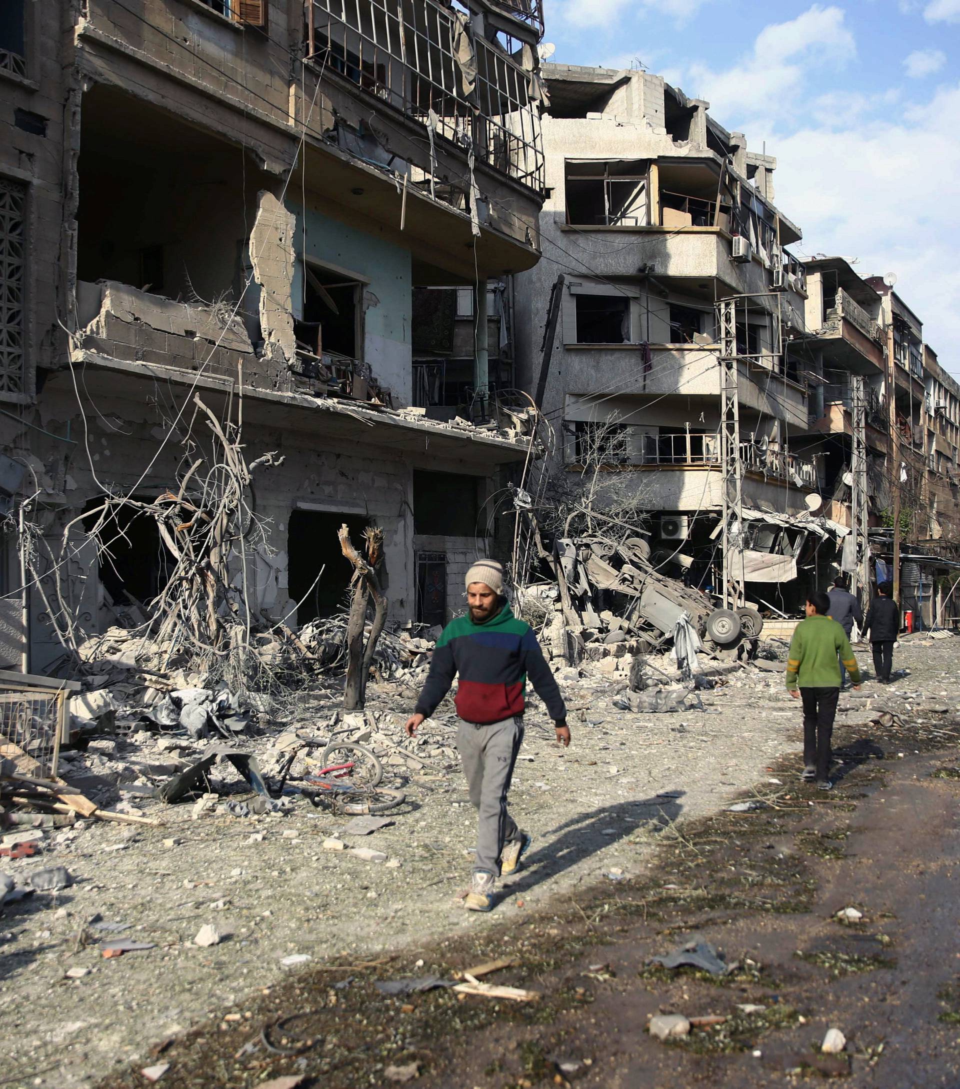 People walk through air raid damage in the besieged town of Douma, Eastern Ghouta, Damascus