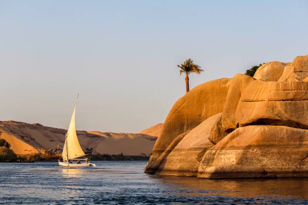 Sailboat on the Nile river at sunset, rock with ancient carvings in the front