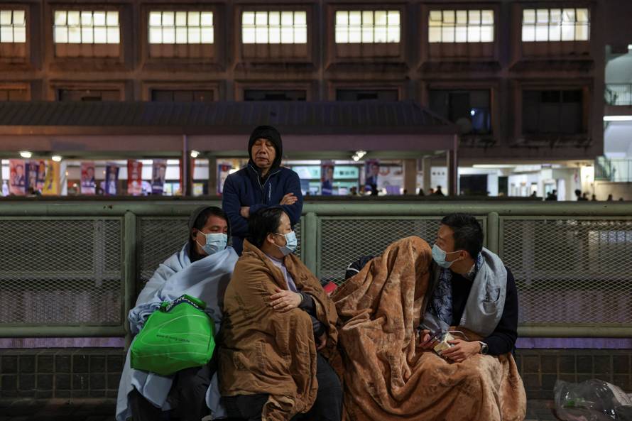 Evacuees wrapped in blankets rest on a nearby platform after a major fire at Wang Fuk Court housing estate, in Tai Po, Hong Kong