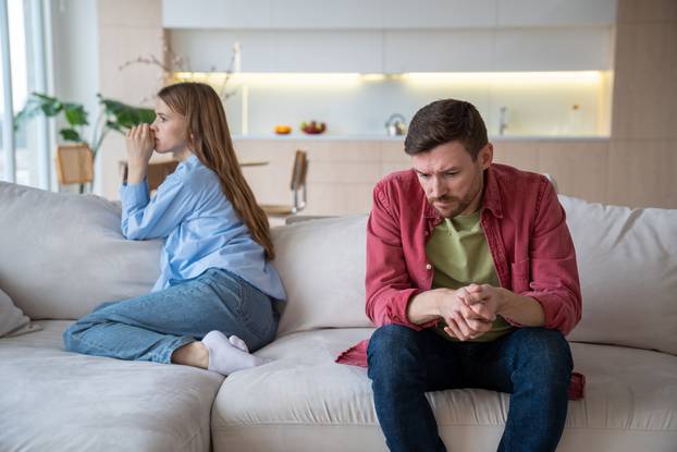 Couple man woman ignoring each other sitting on couch in silence at home turning away.