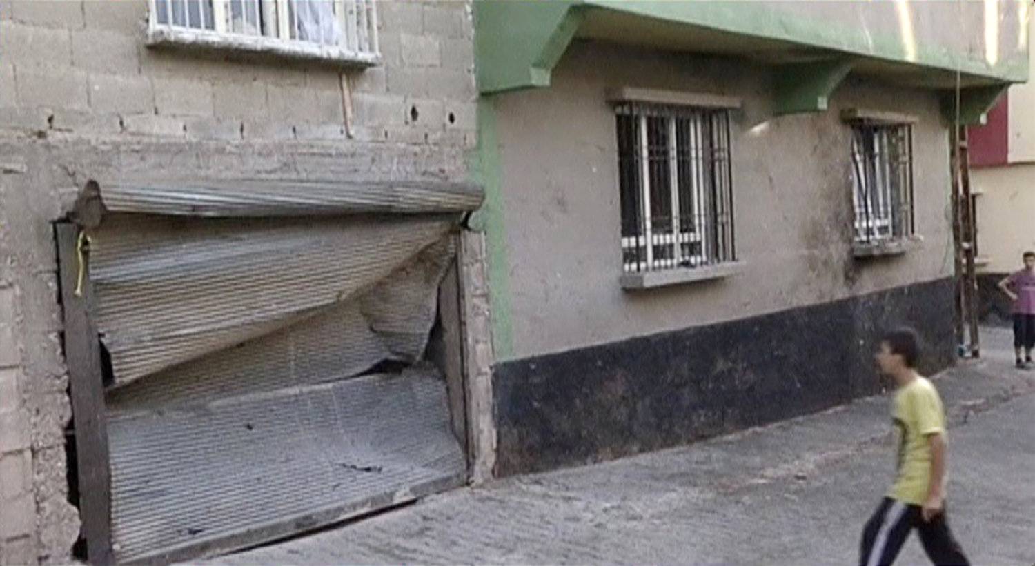 A boy walks in front of a damaged garage door and broken windows at the blast scene of an explosion where a suspected suicide bomber targeted a wedding celebration in the city of Gaziantep