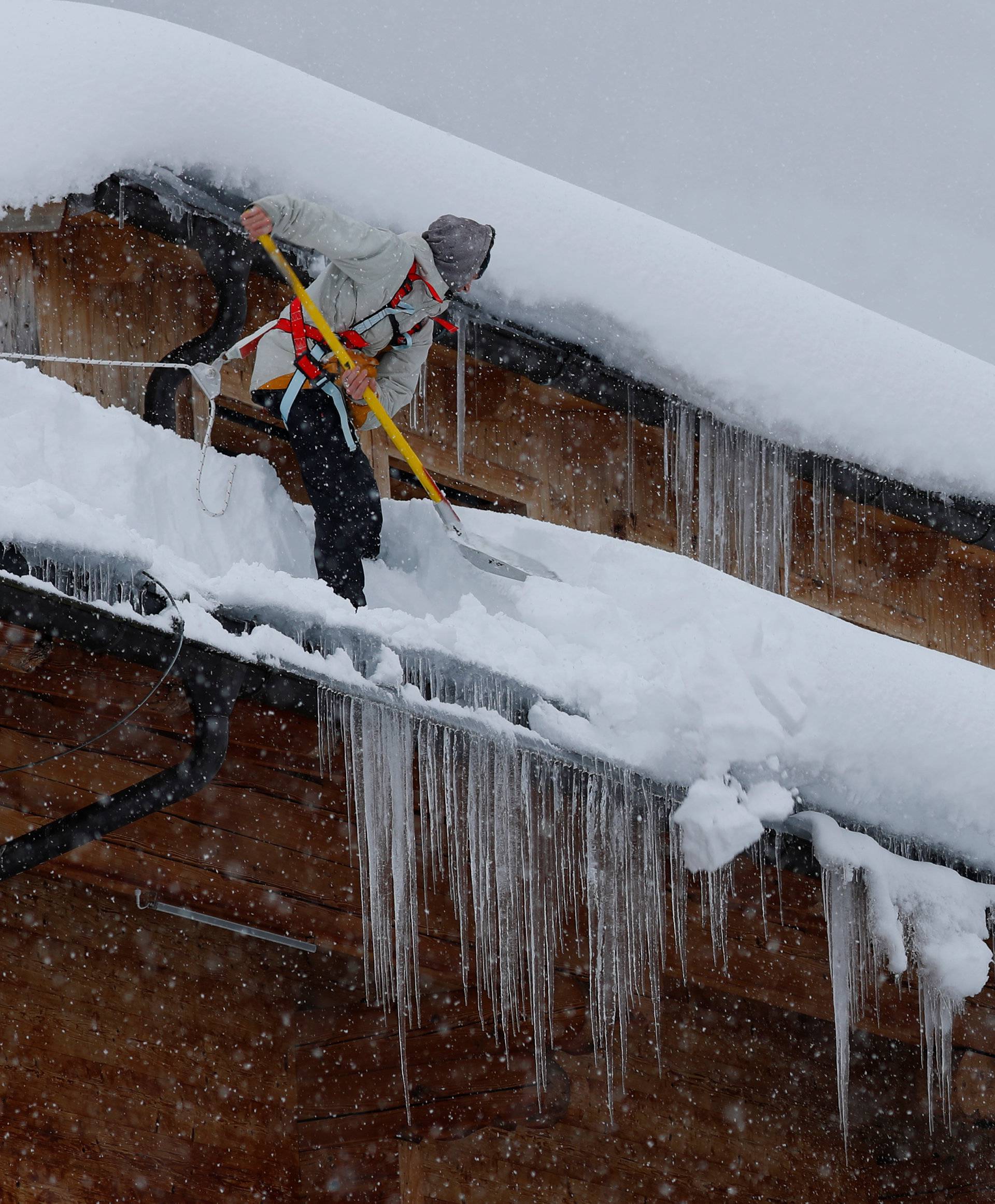 A man shovels snow on a rooftop during heavy snowfall in Flachau