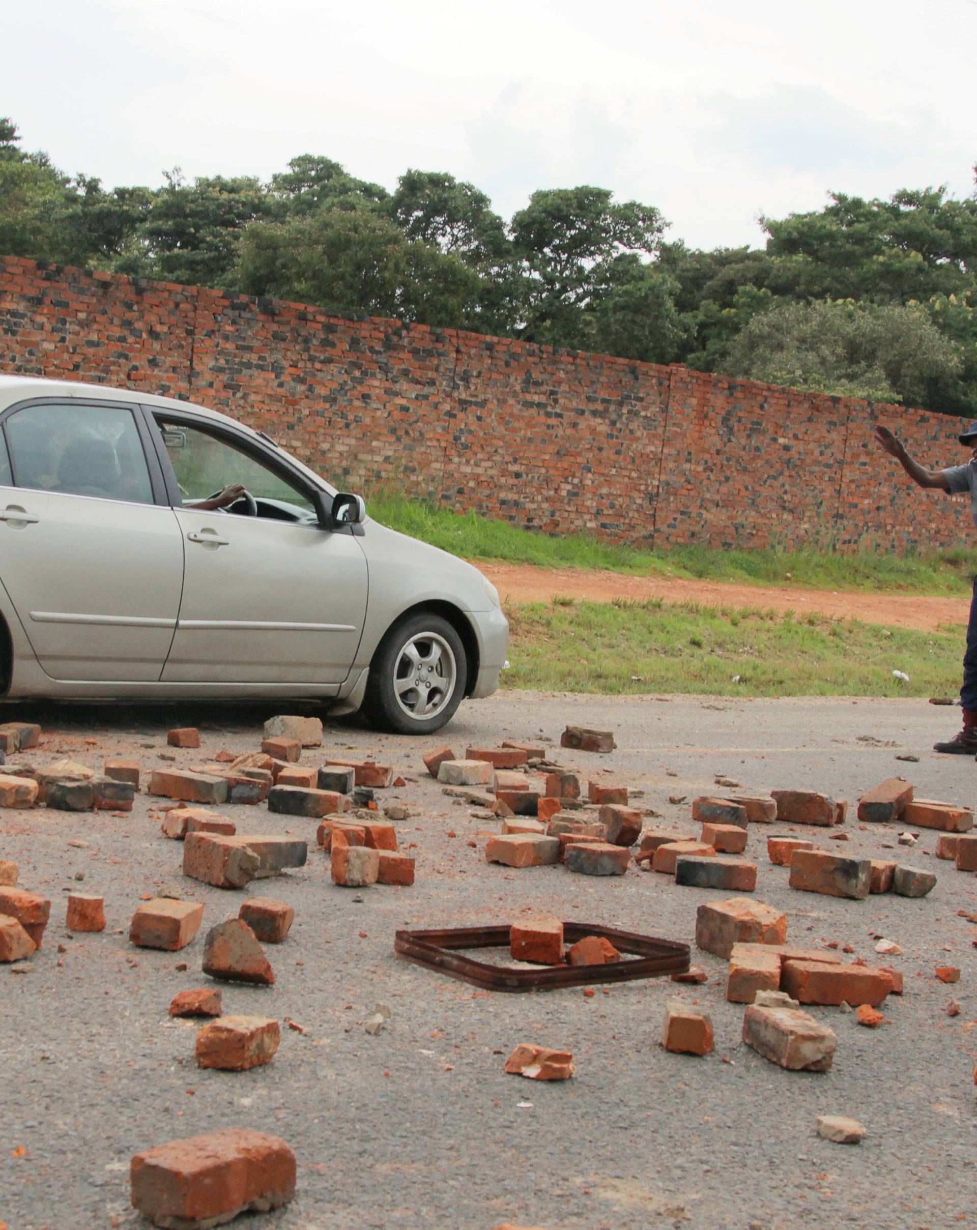 A police officer stops a car on a rock-strewn road during protests in Harare