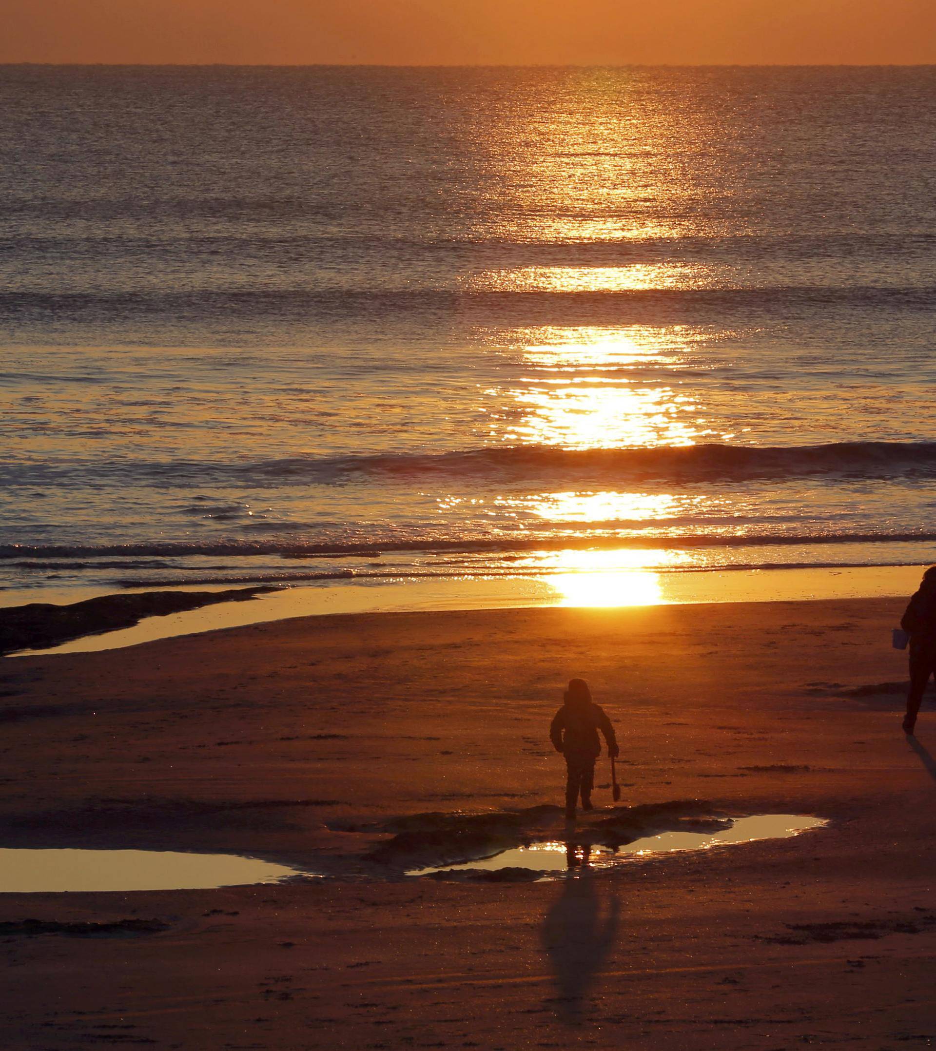 People watch the sun as it sets over the Atlantic Ocean on a cold day in Les Sables d'Olonne 