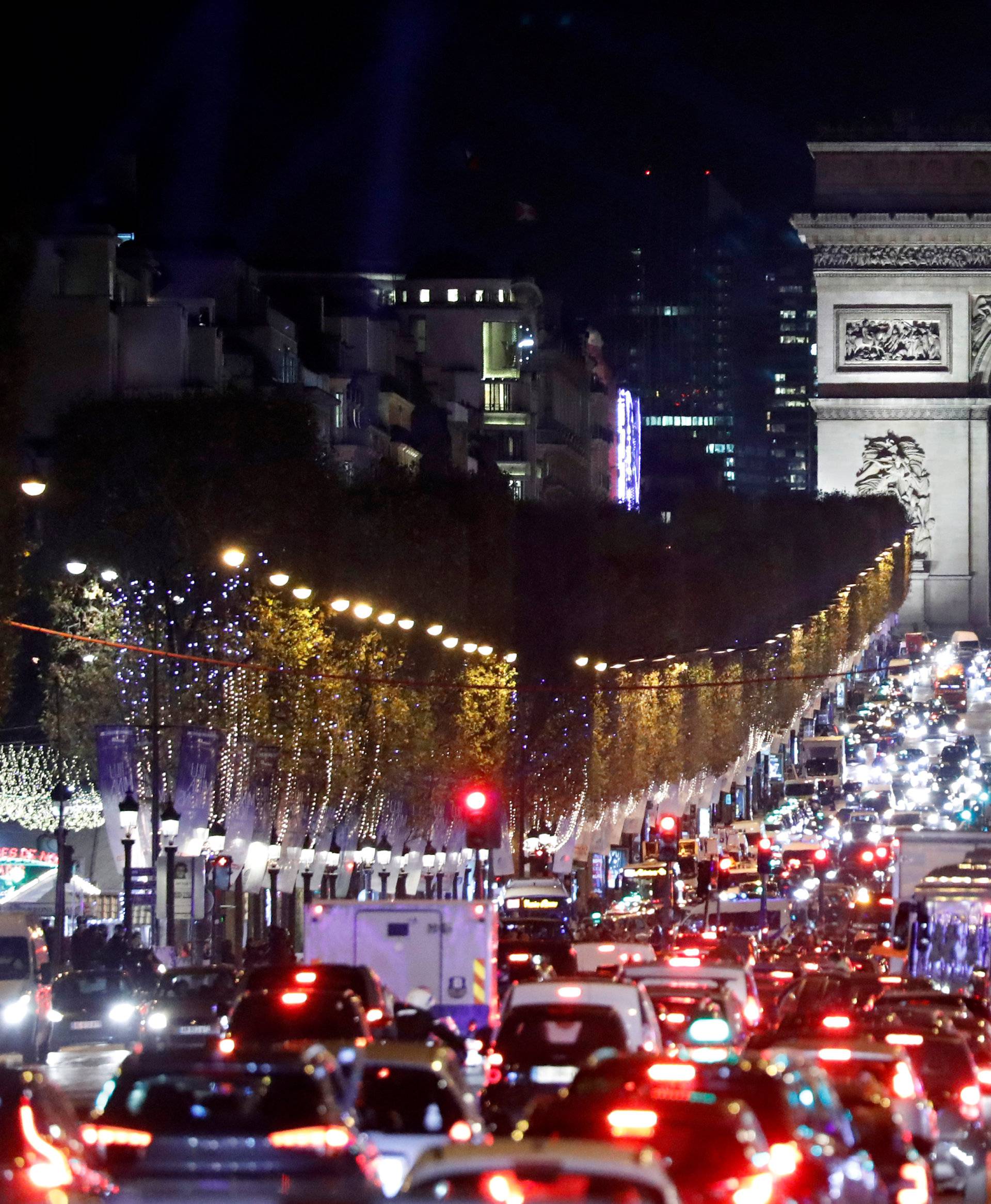 Christmas holiday lights hang from trees to illuminate the Champs Elysees avenue in Paris as rush hour traffic fills the avenue leading up to the Arc de Triomphe