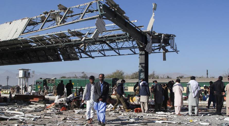People walk amid debris after a bomb blast at a railway station in Quetta