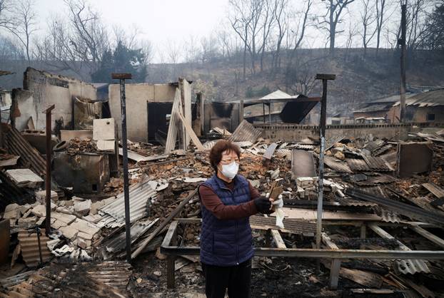 Kun Yeong-nam, 72, uses her mobile phone near her burnt house after a wildfire devastated the area in Uiseong