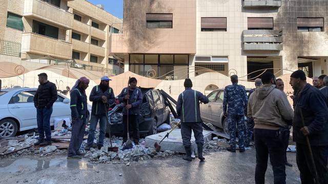 Workers and people stand near a damaged building in the Kafr Sousa district