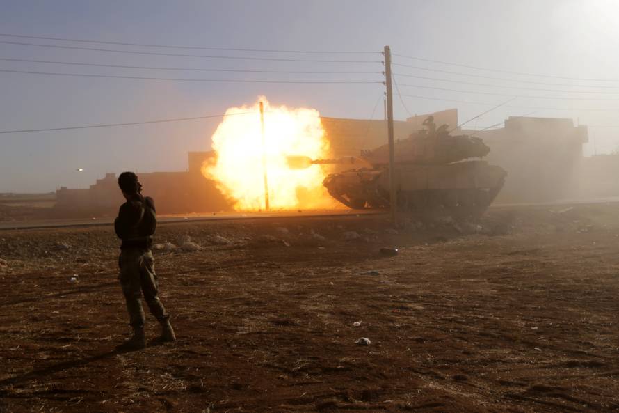 A rebel fighter stands near a Turkish tank as it fires towards Guzhe village, northern Aleppo countryside