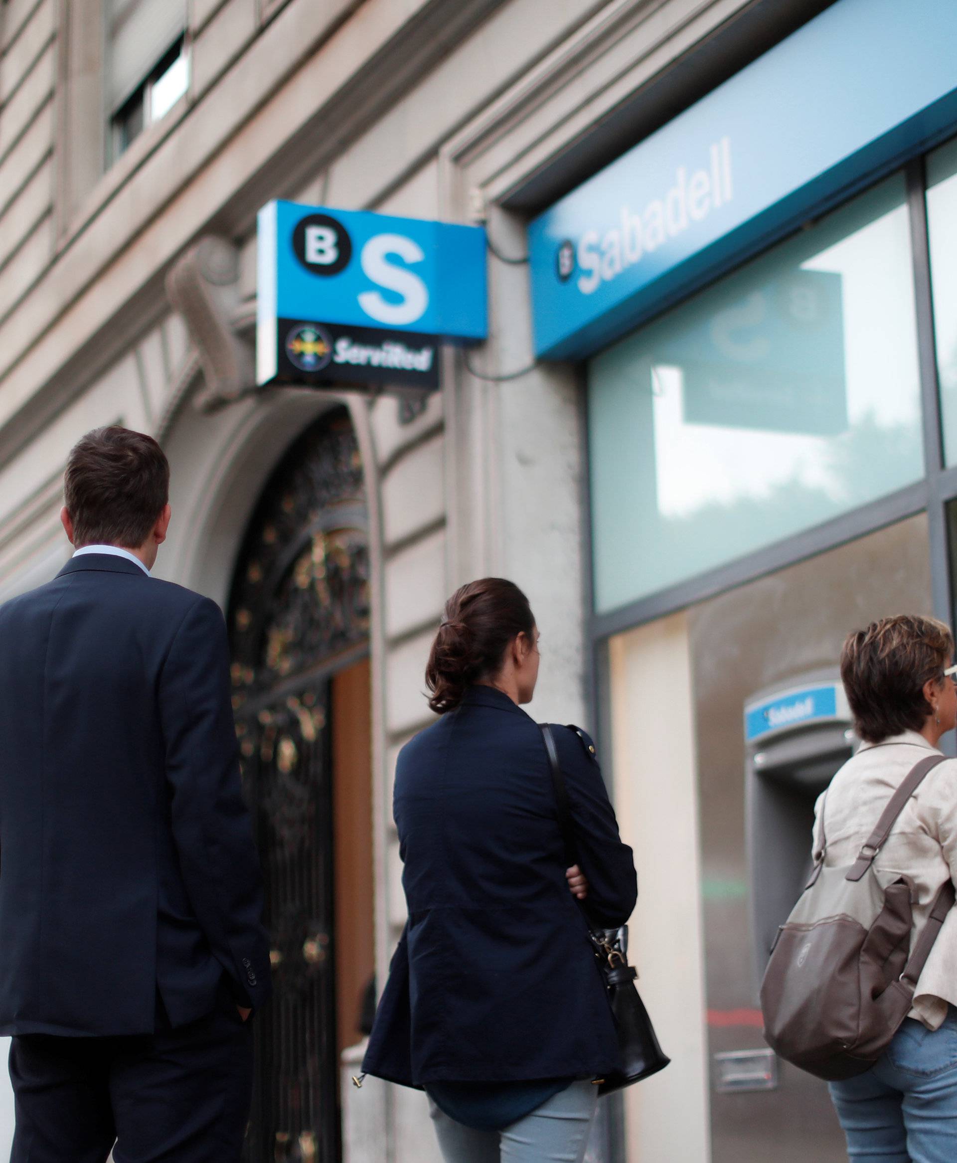 People line up at a cashpoint of Sabadell bank branch to withdraw money as part of an action to protest the transfer of the bank's headquarters out of Barcelona