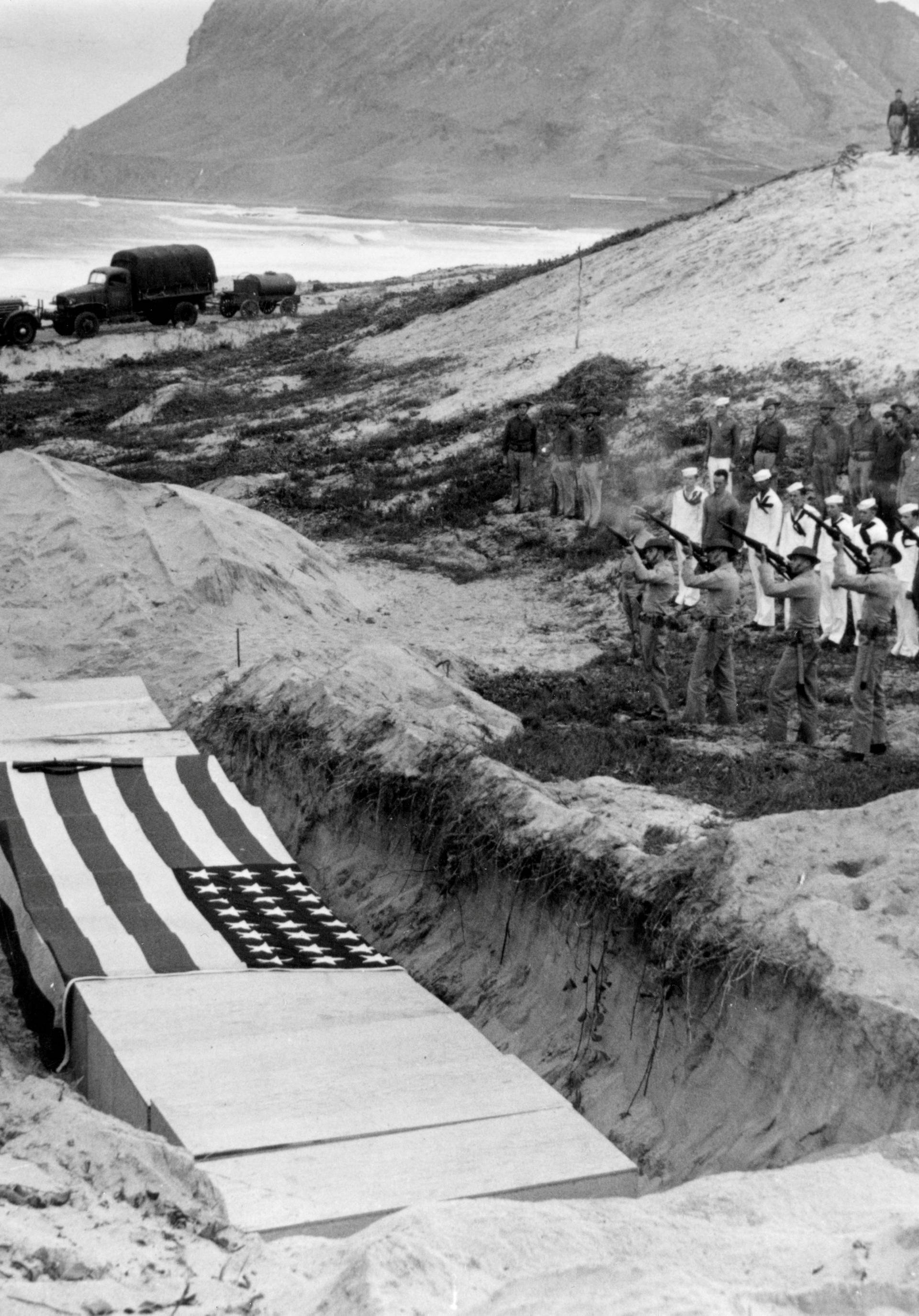 Archive photo of a Marine rifle squad firing a volley over the bodies of 15 officers and men killed the previous day at Pearl Harbor