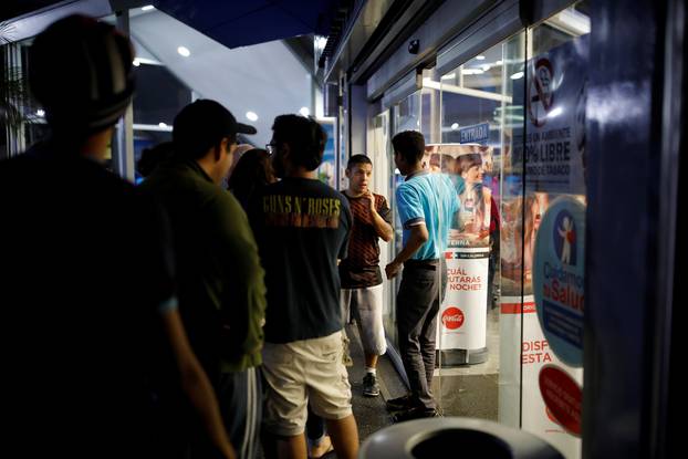 People queue outside a pharmacy to try to buy goods during a blackout in Caracas