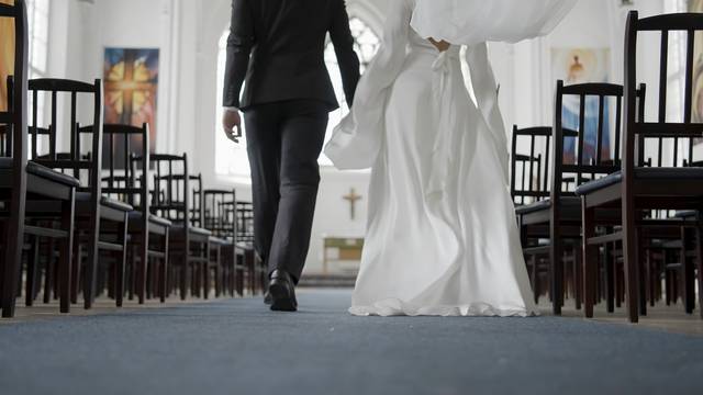 Beautiful newlyweds walking down aisle. Action. Rear view of couple of newlyweds in church. Newlyweds walk down aisle at wedding rehearsal