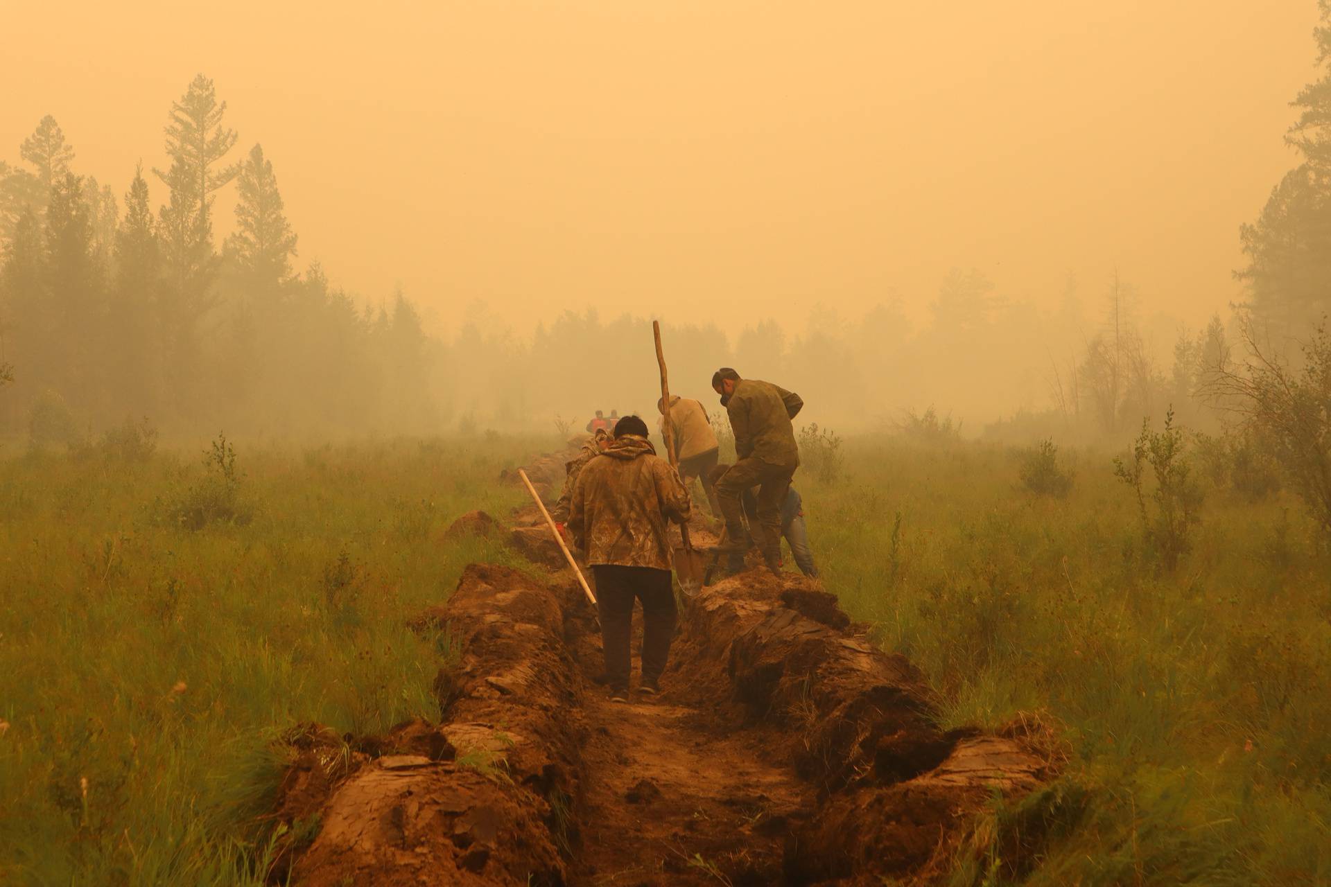 Firefighters and volunteers dig a control line during the work on extinguishing a forest fire in Yakutia