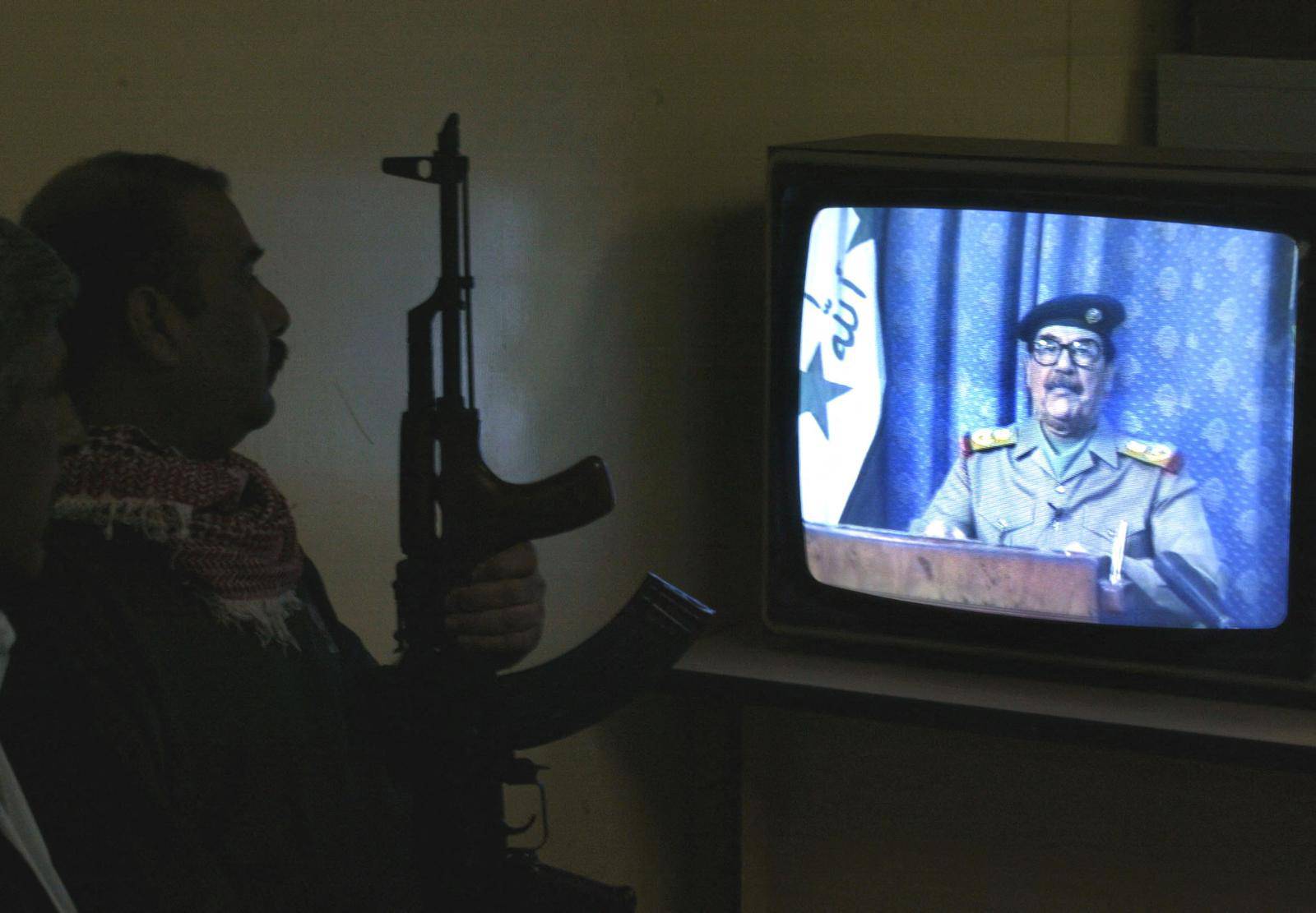 FILE PHOTO: Armed Iraqi man watches Iraqi President Saddam Hussein on TV in Baghdad