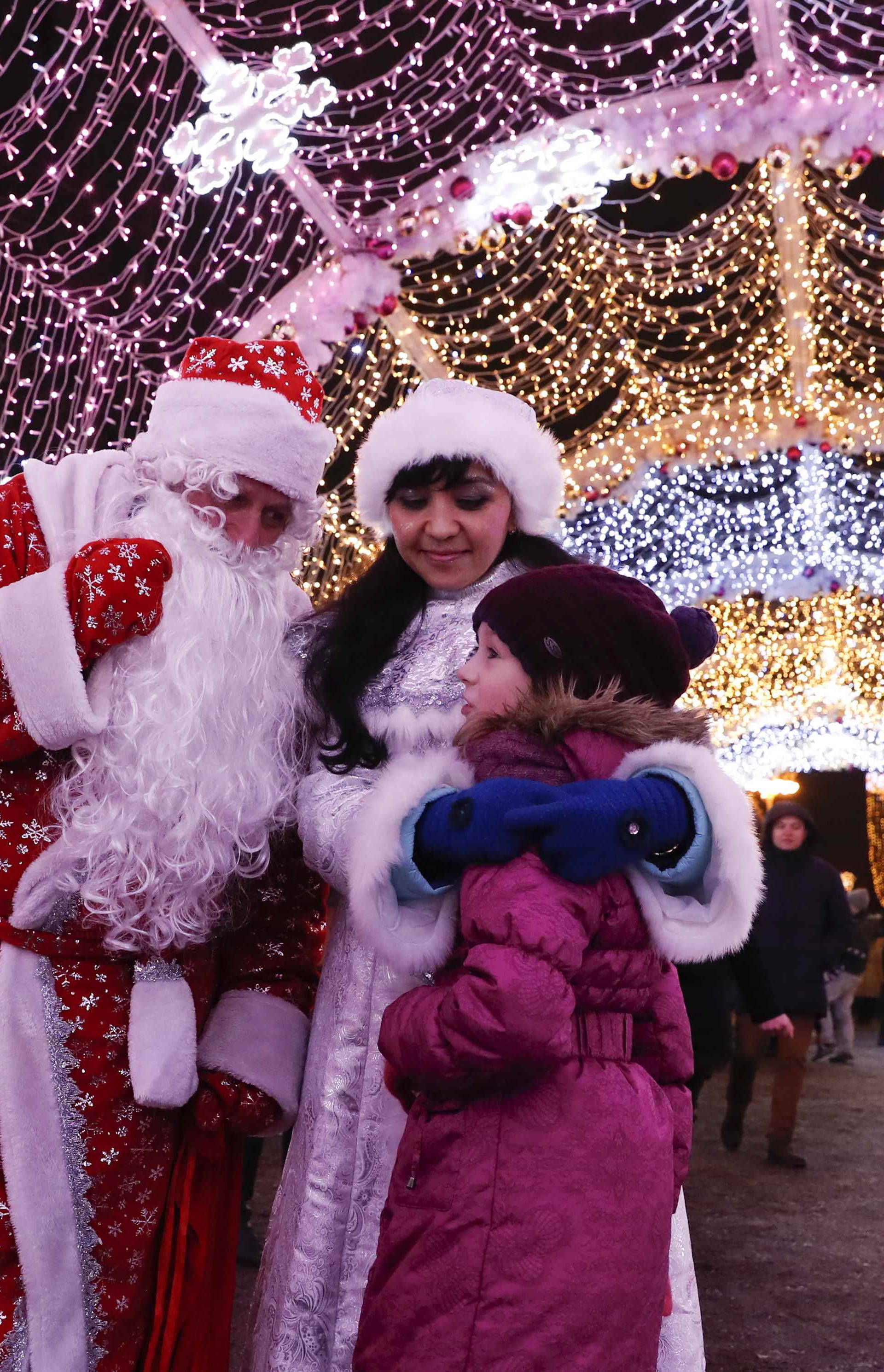 People dressed as Father Frost, the Russian equivalent of Santa Claus, and Snow Maiden talk with a girl as they stand under festive decorations for the upcoming New Year and Christmas season in central Moscow