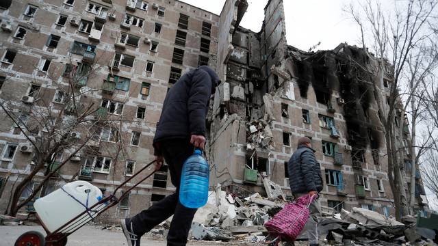 Local residents walk past a damaged apartment building in Mariupol