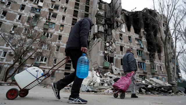 Local residents walk past a damaged apartment building in Mariupol