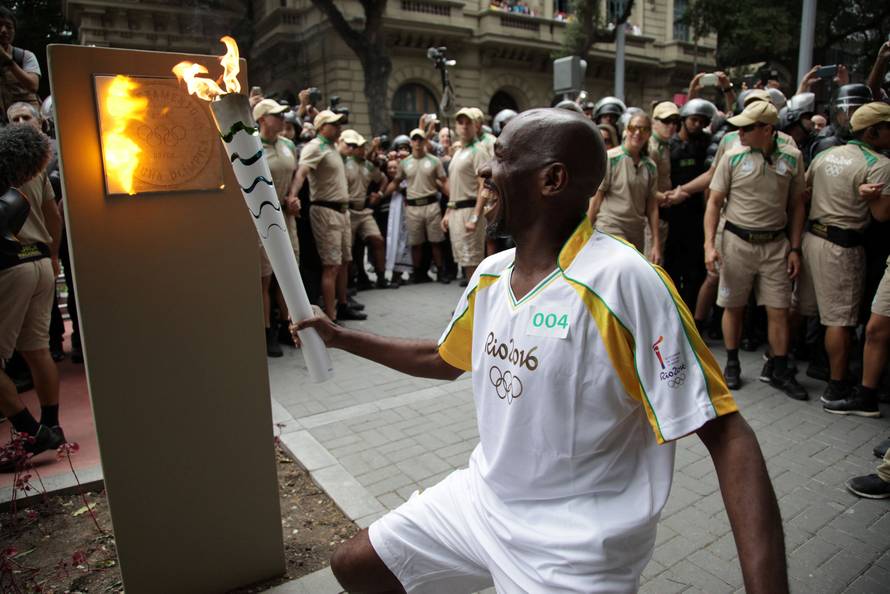 Street sweeper Renato Sorriso smiles while lighting the first of five posts with the Olympic torch in Rio de Janeiro