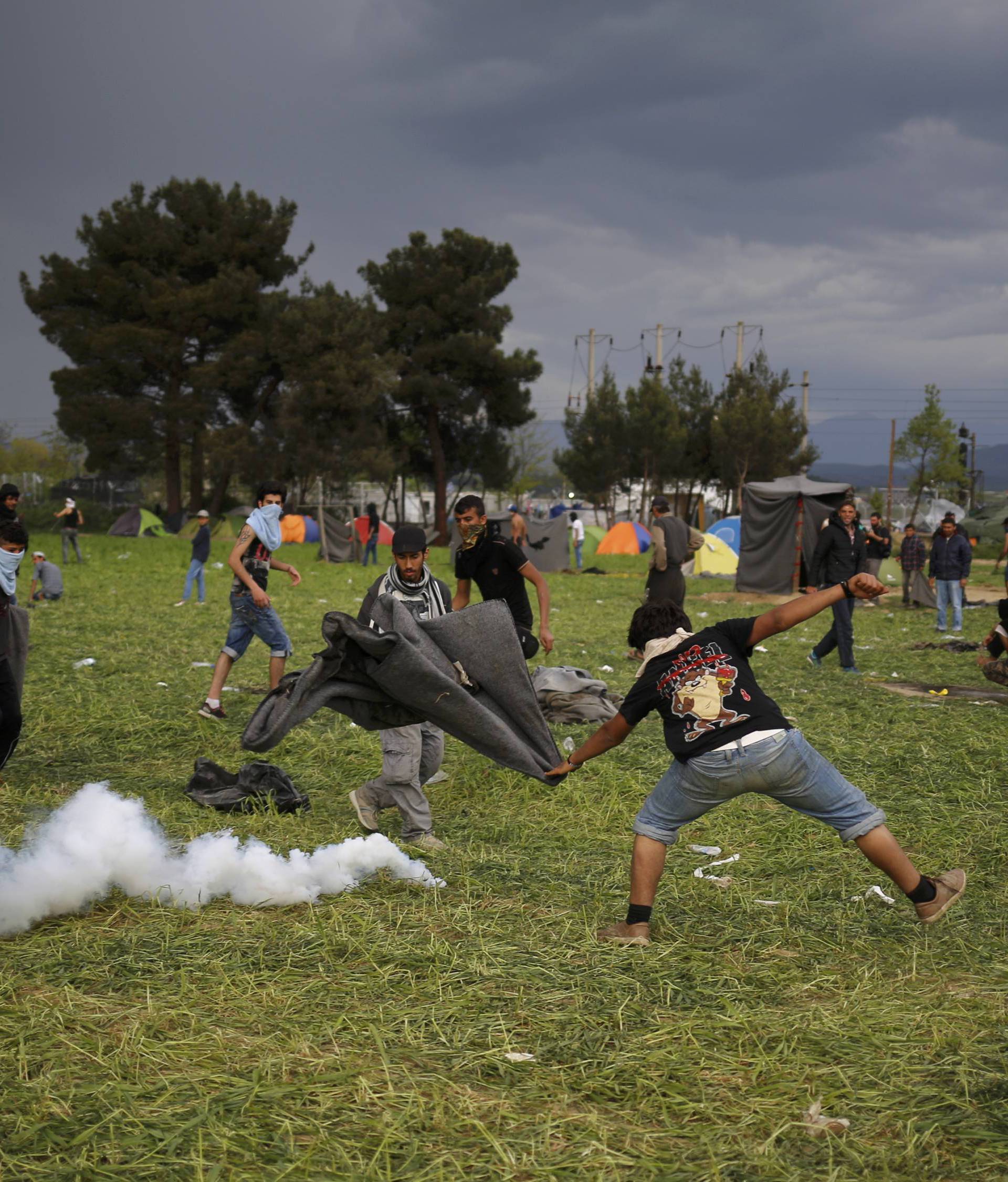 A protesting migrant tries to extinguish a teargas canister during clashes at the Greek-Macedonian border near Idomeni