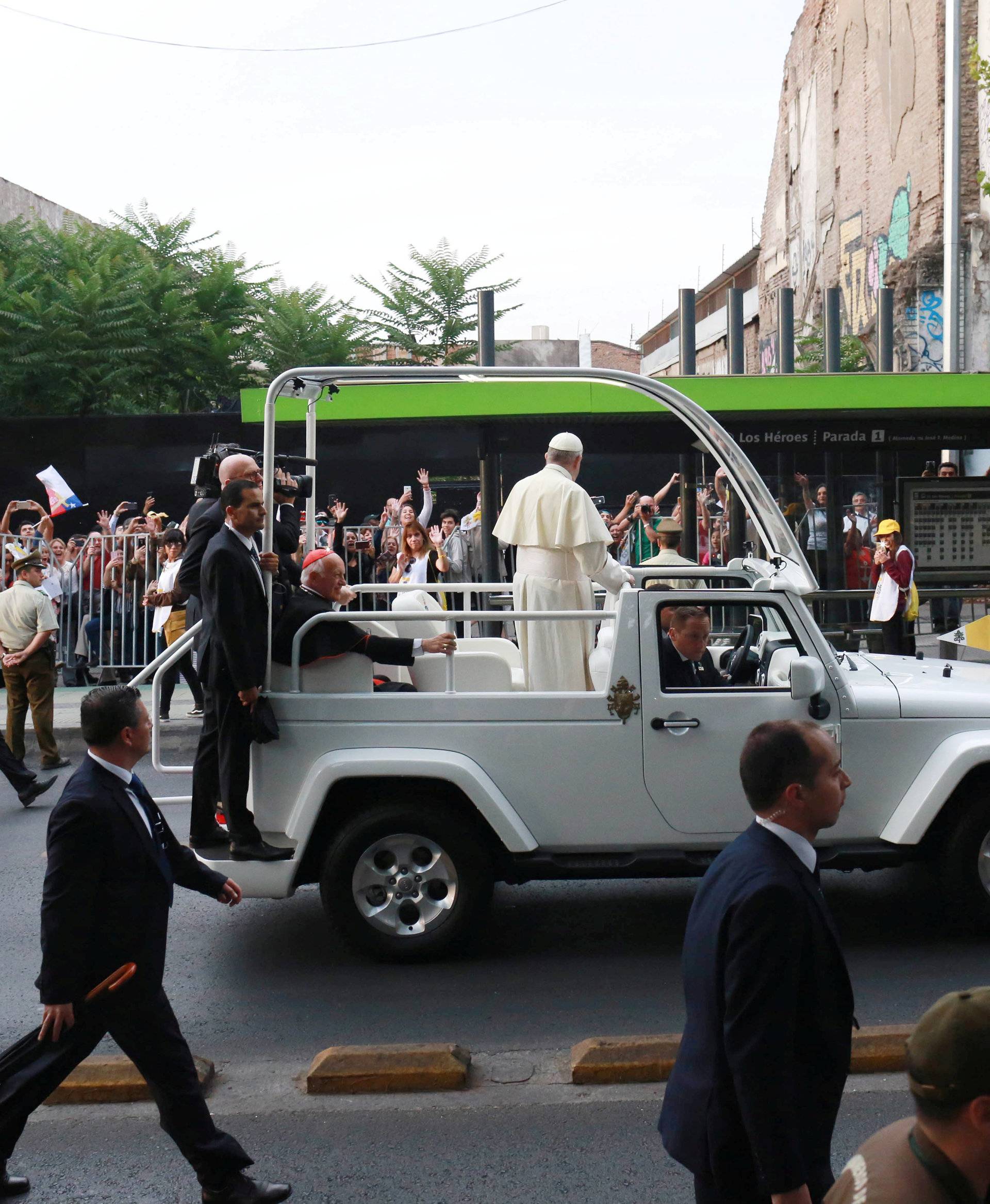 Police and security personnel run next to Pope Francis as he drives through Santiago