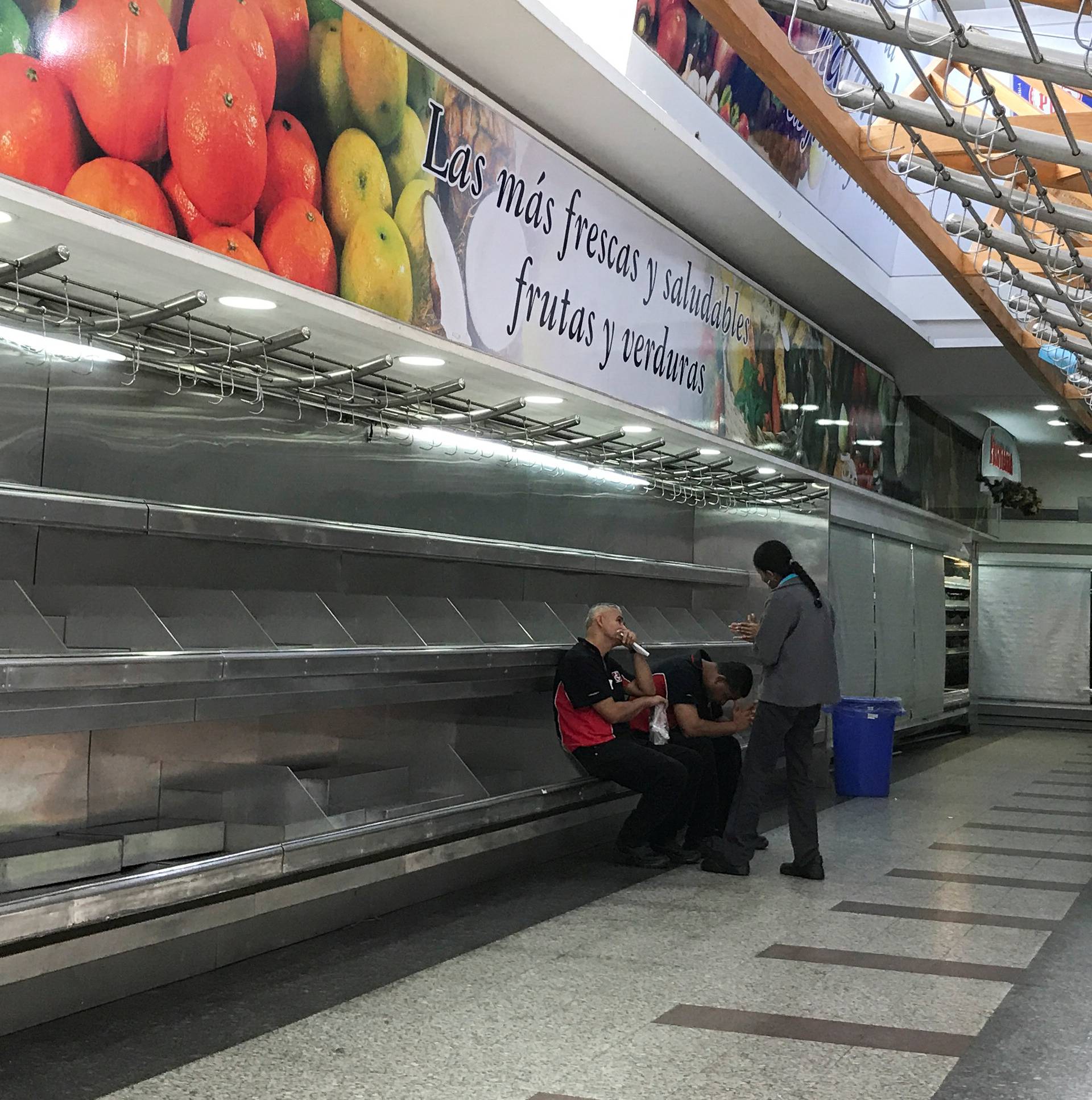Workers sit on empty shelves at the fruit and vegetables area in a supermarket in Caracas
