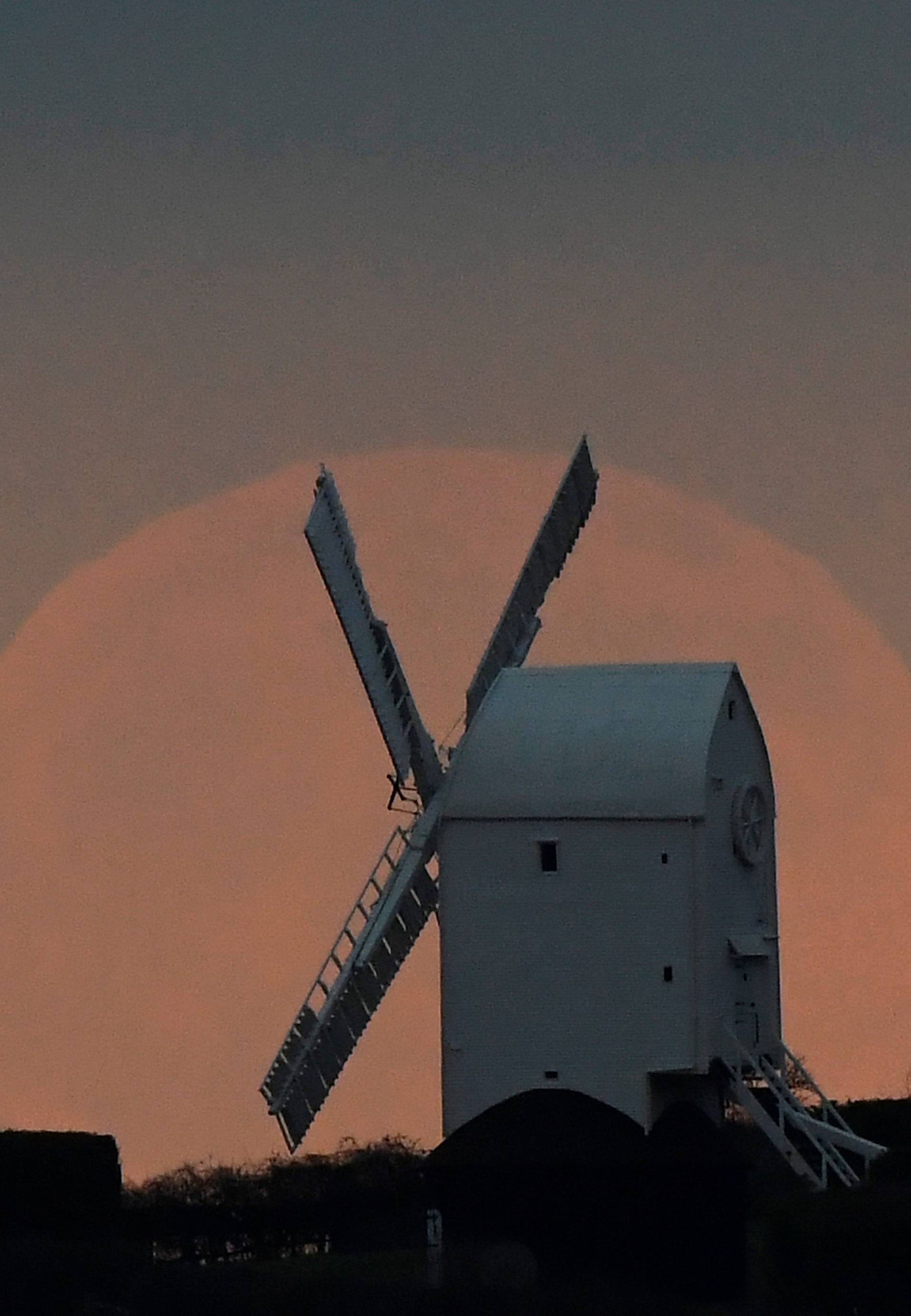 The full moon is seen rising behind a windmill on the Sussex Downs near Brighton, Britain