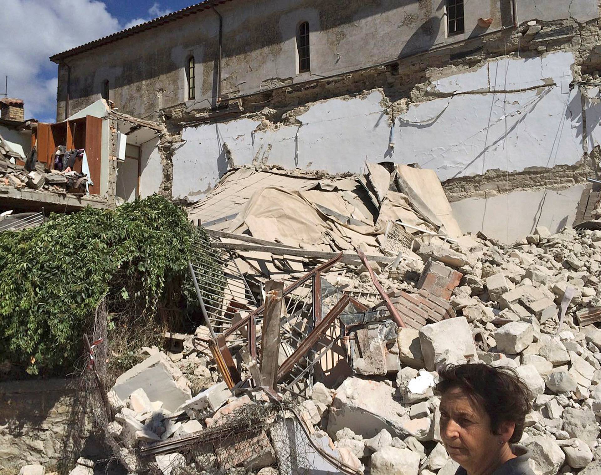 A woman stands in front of a collapsed house following an earthquake in Accumoli di Rieti