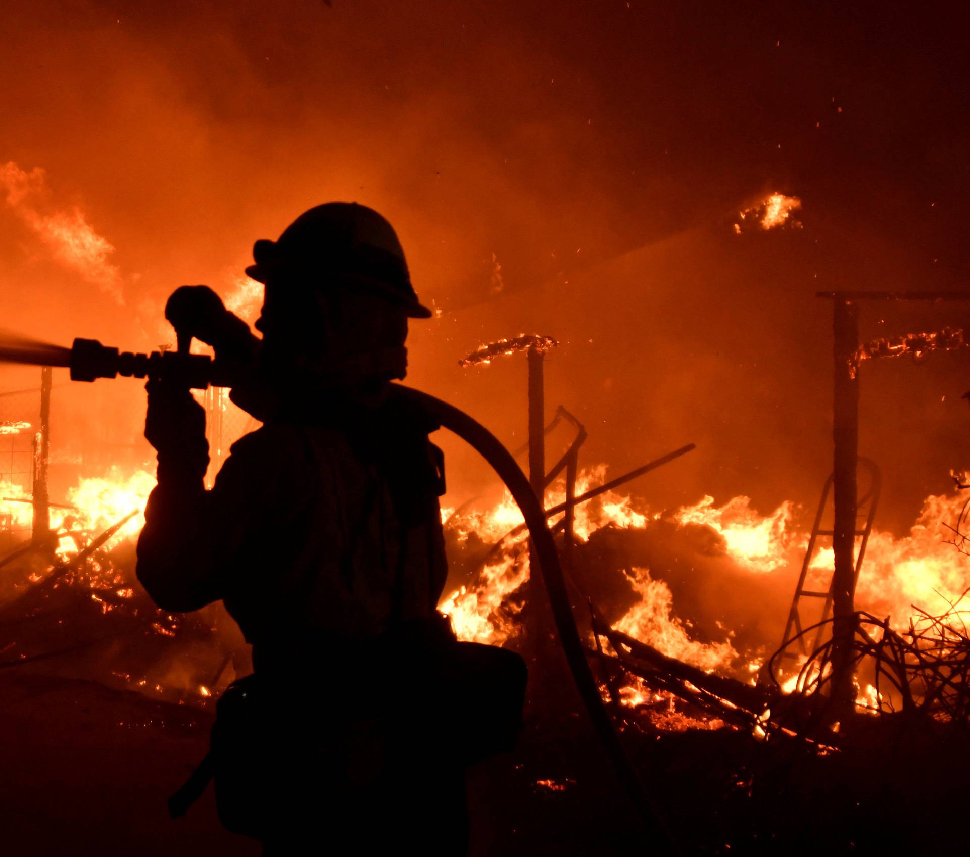 A firefighter hoses down a property engulfed in flames during the Woolsey Fire in Malibu