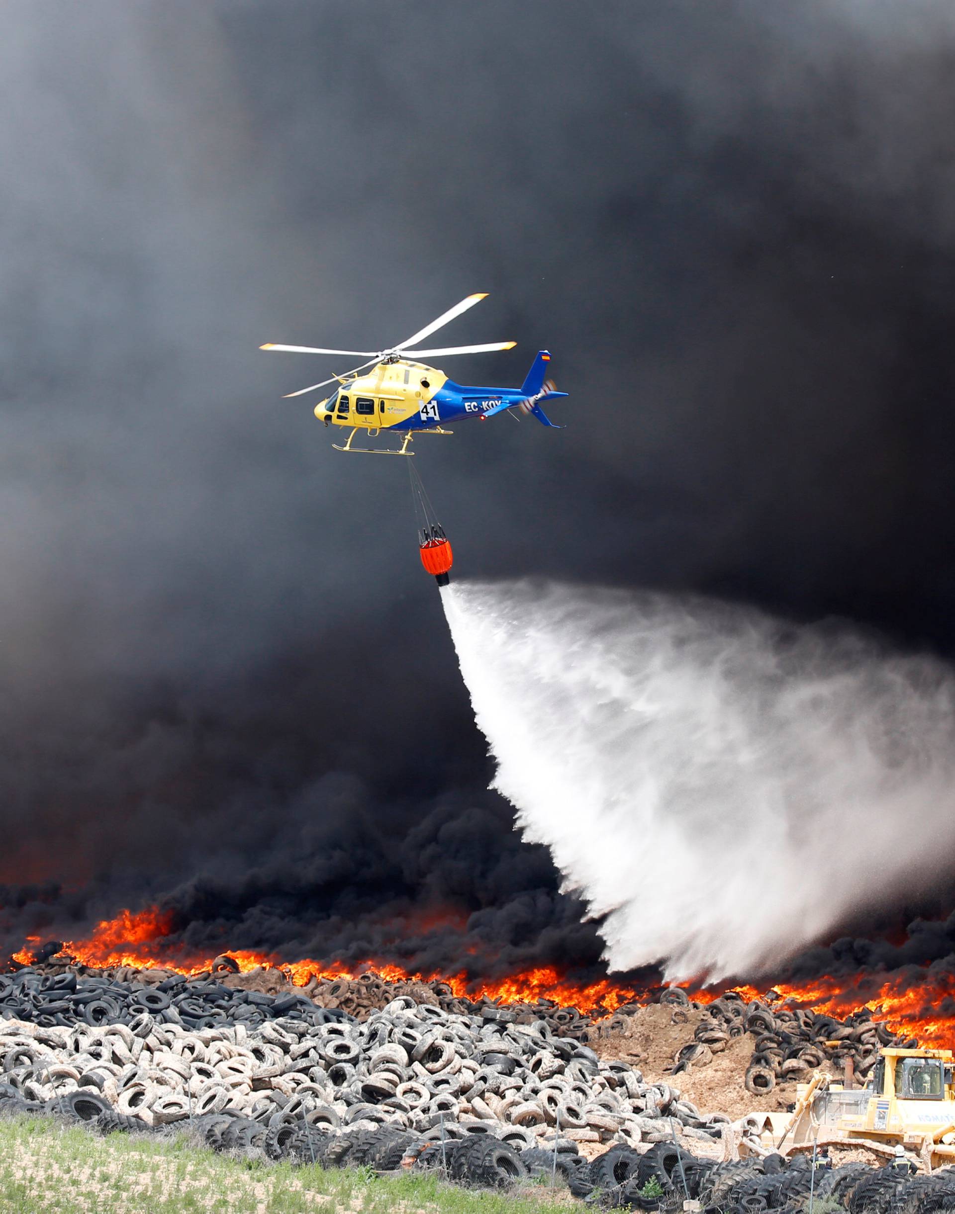 An helicopter throws water over a fire at a tire dump near a residential development in Sesena