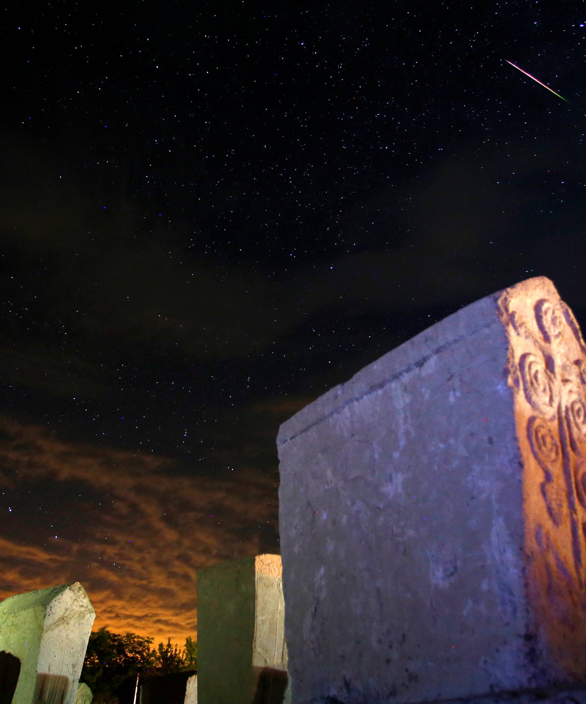 A meteor streaks past stars in the night sky above medieval tombstones in Radmilje near Stolac, south of Sarajevo