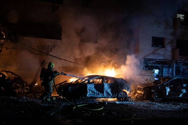 An Israeli firefighter works to put out a fire on a car at the site of a projectile impact, in Tel Aviv