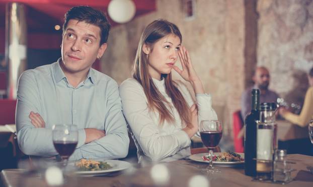 Young emotional couple quarreled in restaurant sitting at served