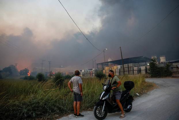 People watch a fire at a cement factory sparked by a nearby wildfire, in Patras