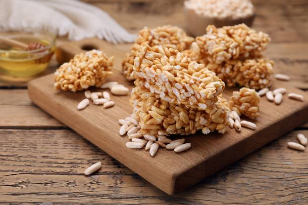 Board with puffed rice pieces (kozinaki) on wooden table, space 