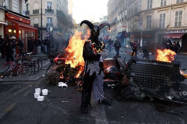 A demonstrator wearing a costume stands in front of burning flames, in Paris