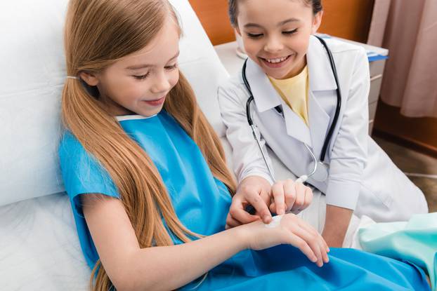 girl doctor putting medical plaster on hand of little patient