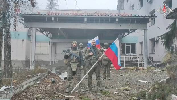 Russian service members hold flags in front of a hospital in Kupiansk